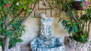 A stone statue of a reclining figure on a rock base, surrounded by lush greenery and a stone wall. - Apartments Aura - Comfort Studio Apartment f with shared swimming pool (Dubrovnik)