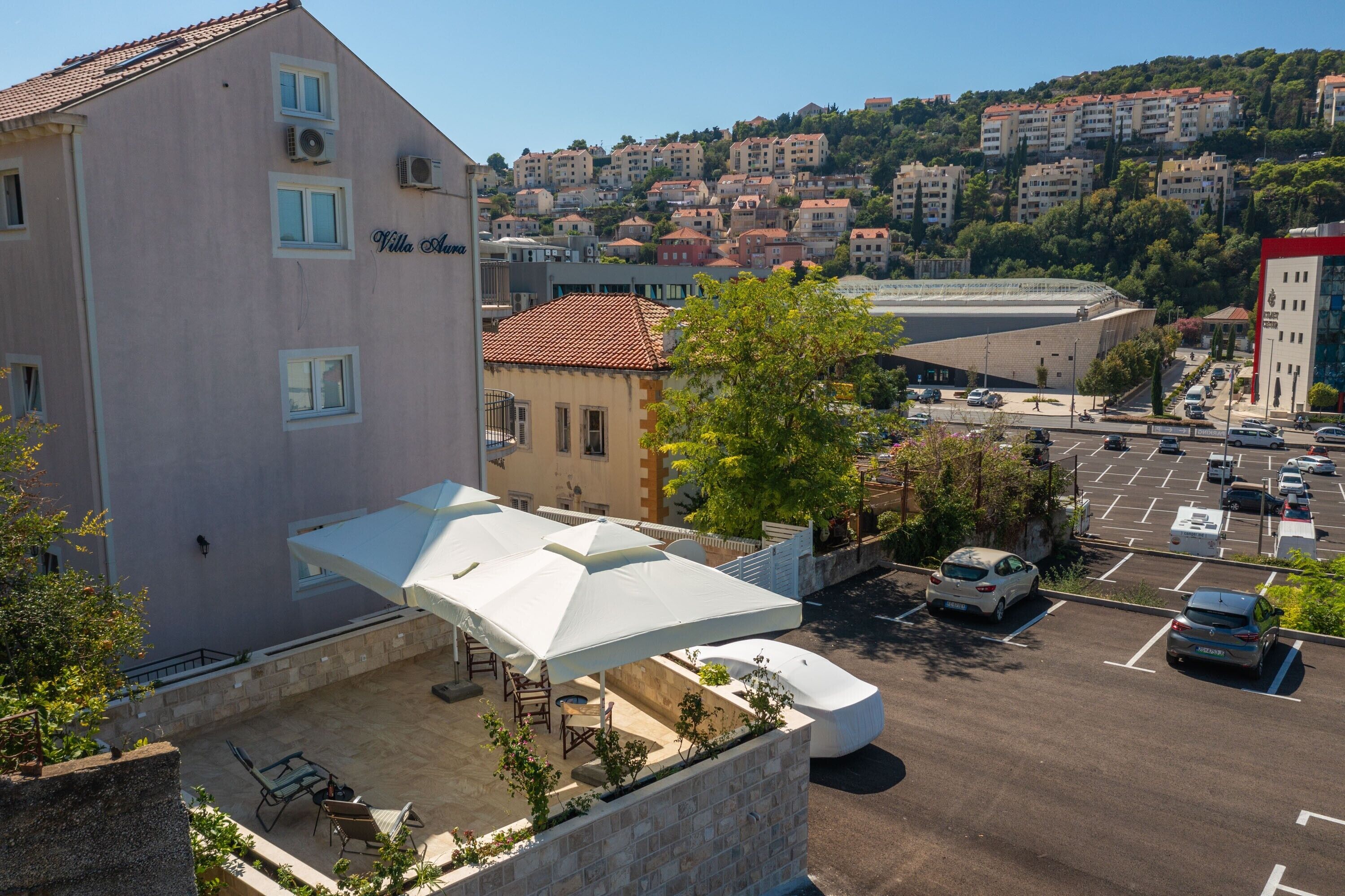 Ein Hotel mit einer Terrasse, Sitzgelegenheiten im Freien und einem Parkplatz.