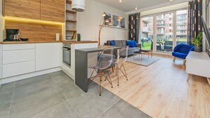 Un appartement moderne comprenant une cuisine, un coin repas et un salon. Il dispose d’une grande fenêtre offrant une vue sur la ville.