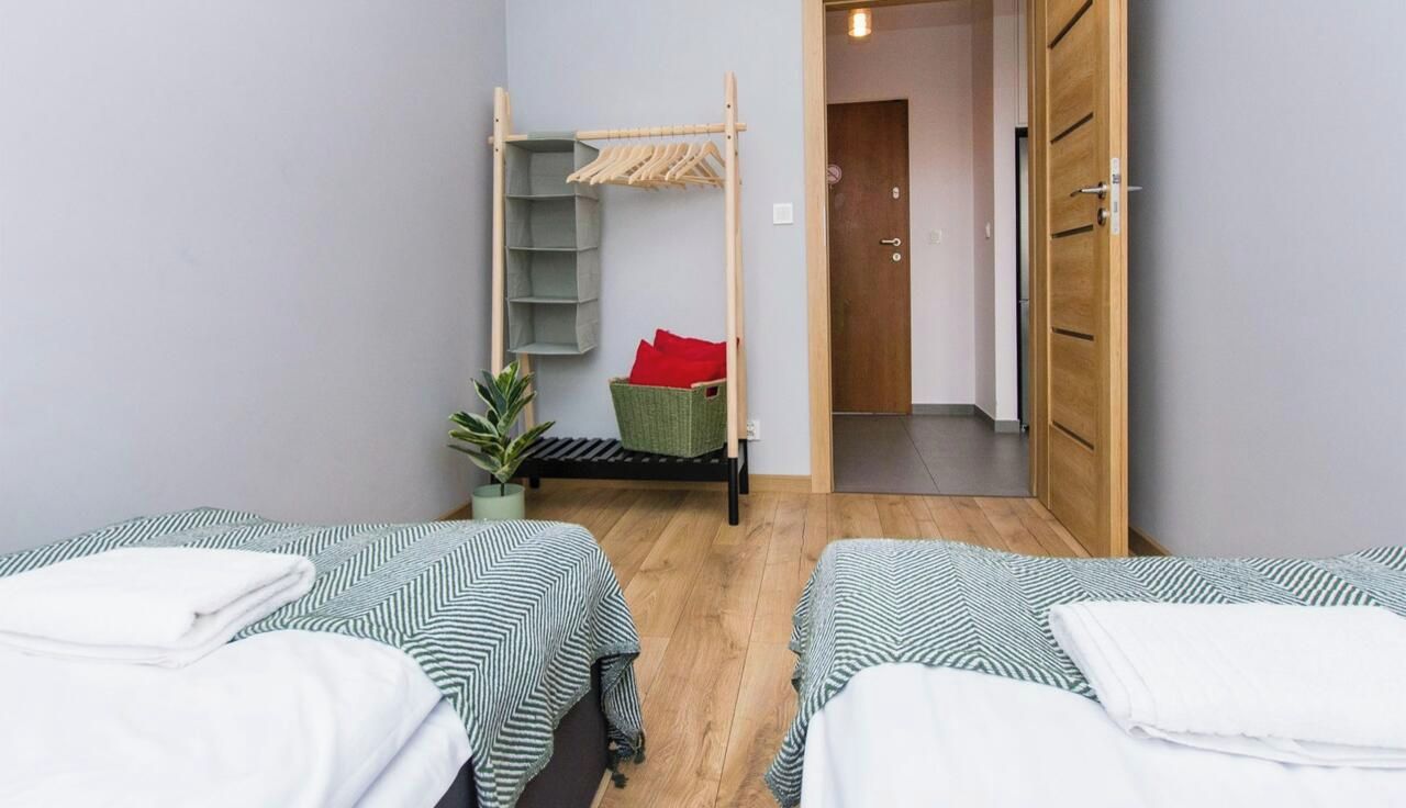 Une chambre avec deux lits, une armoire en bois, un étendoir et une petite plante.