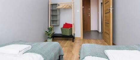 Une chambre avec deux lits, une armoire en bois, un étendoir et une petite plante.