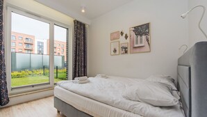 Un dormitorio con cama, ventana con cortinas y vistas a edificios.