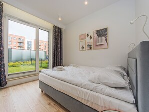 Een slaapkamer met een bed, een raam met gordijnen en uitzicht op gebouwen.