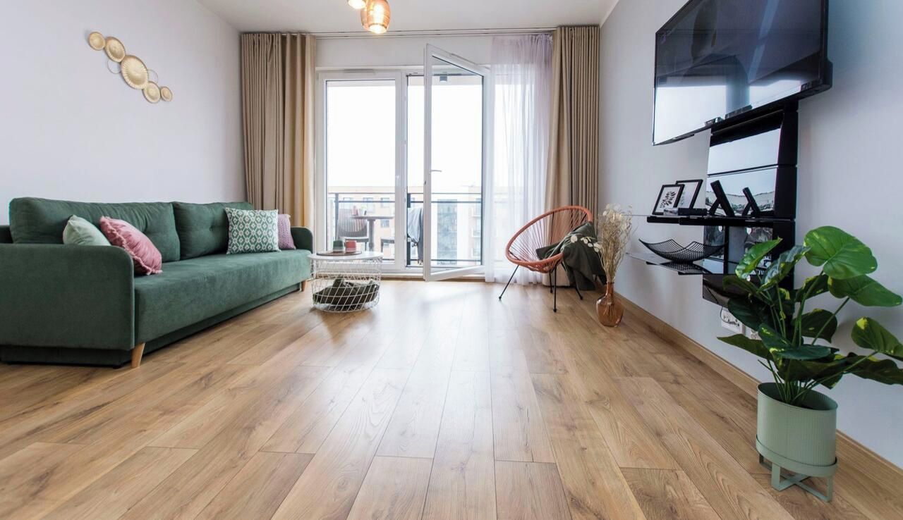 Uma sala de estar moderna com um sofá verde, uma poltrona vermelha, uma TV na parede e uma varanda com cortinas.