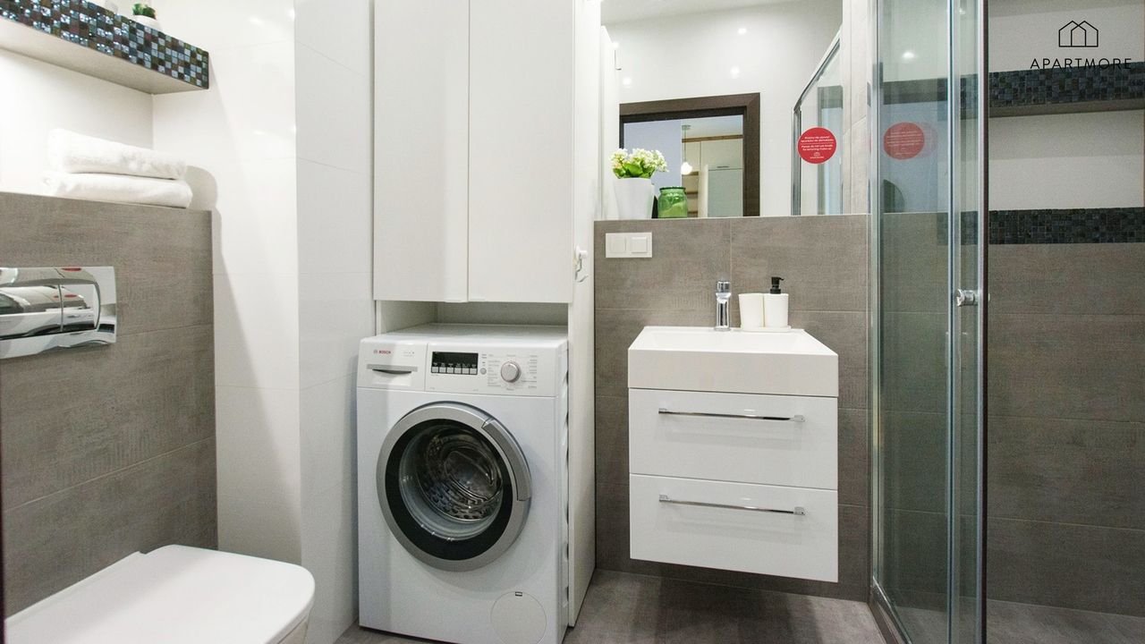 A compact bathroom with a washing machine, a toilet, a sink with a mirror, and a shower area.