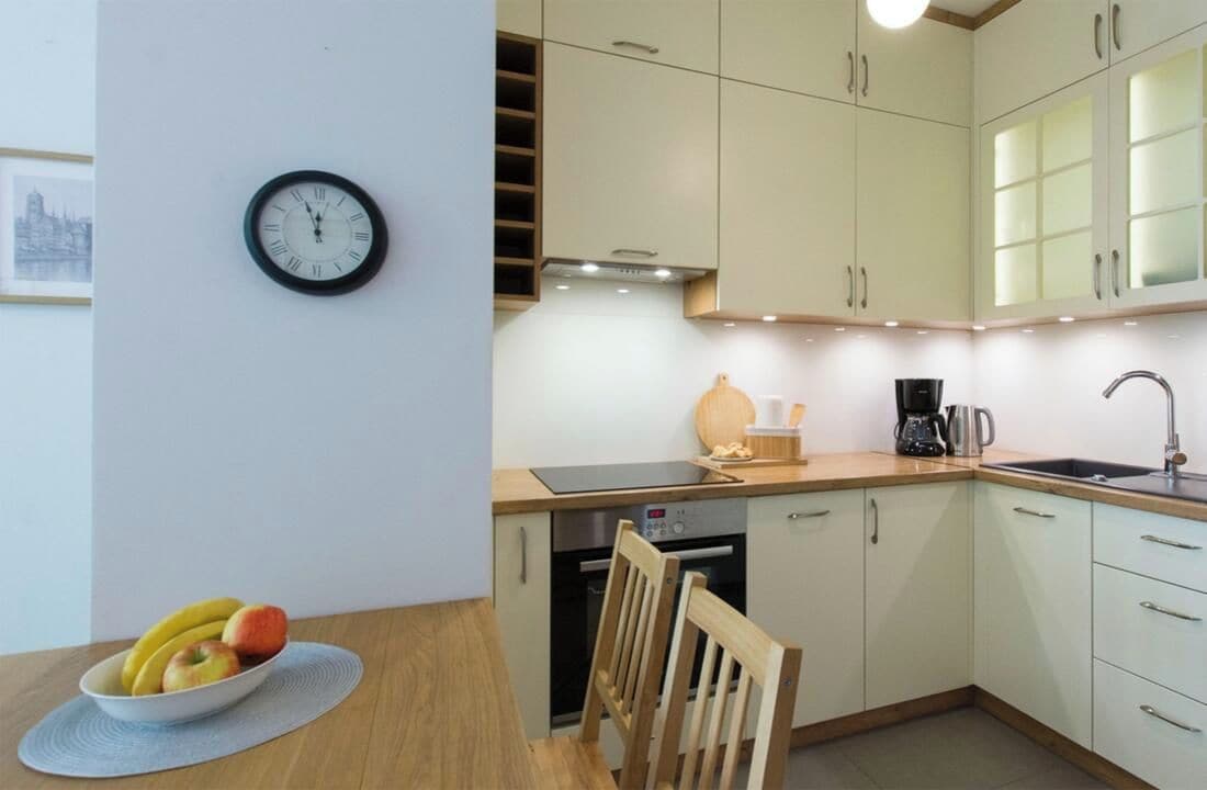A kitchen with a clock, a bowl of fruit, and a coffee maker.