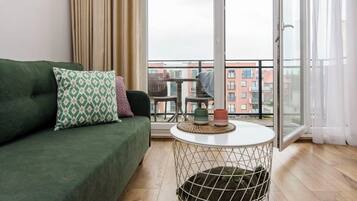 A modern living room with a green sofa, a patterned pillow, a small round table with a woven coaster, and a pet bed.