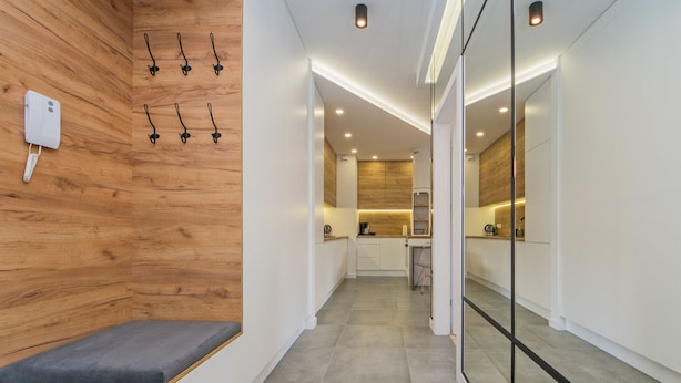 Un couloir d’hôtel moderne avec un mur en bois, un coin salon et une cuisine en arrière-plan.