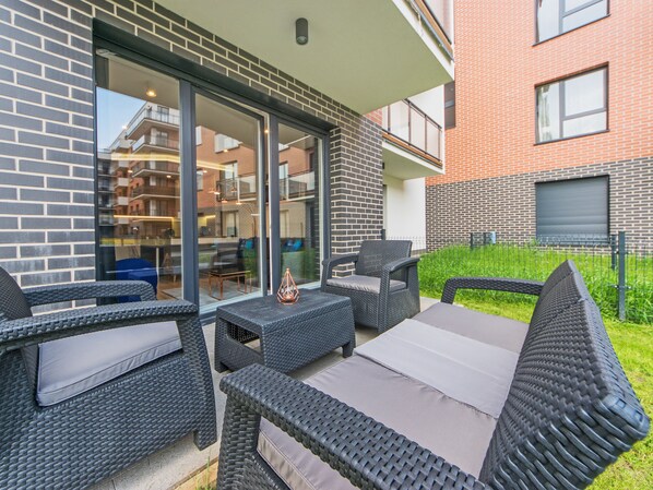 Een terras met rieten meubilair en een glazen deur die leidt naar een balkon.