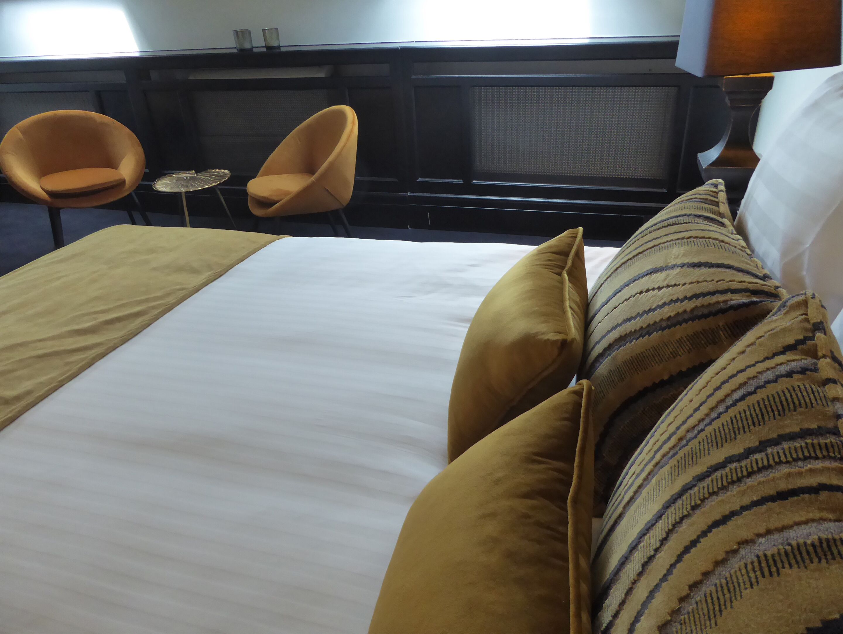 Habitación de hotel con una cama grande, dos sillones, una mesita redonda y una ventana con persianas.