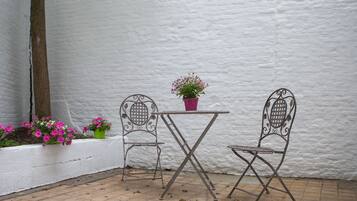 Een terras met twee metalen stoelen en een kleine tafel, omgeven door witte muren en plantenbakken.