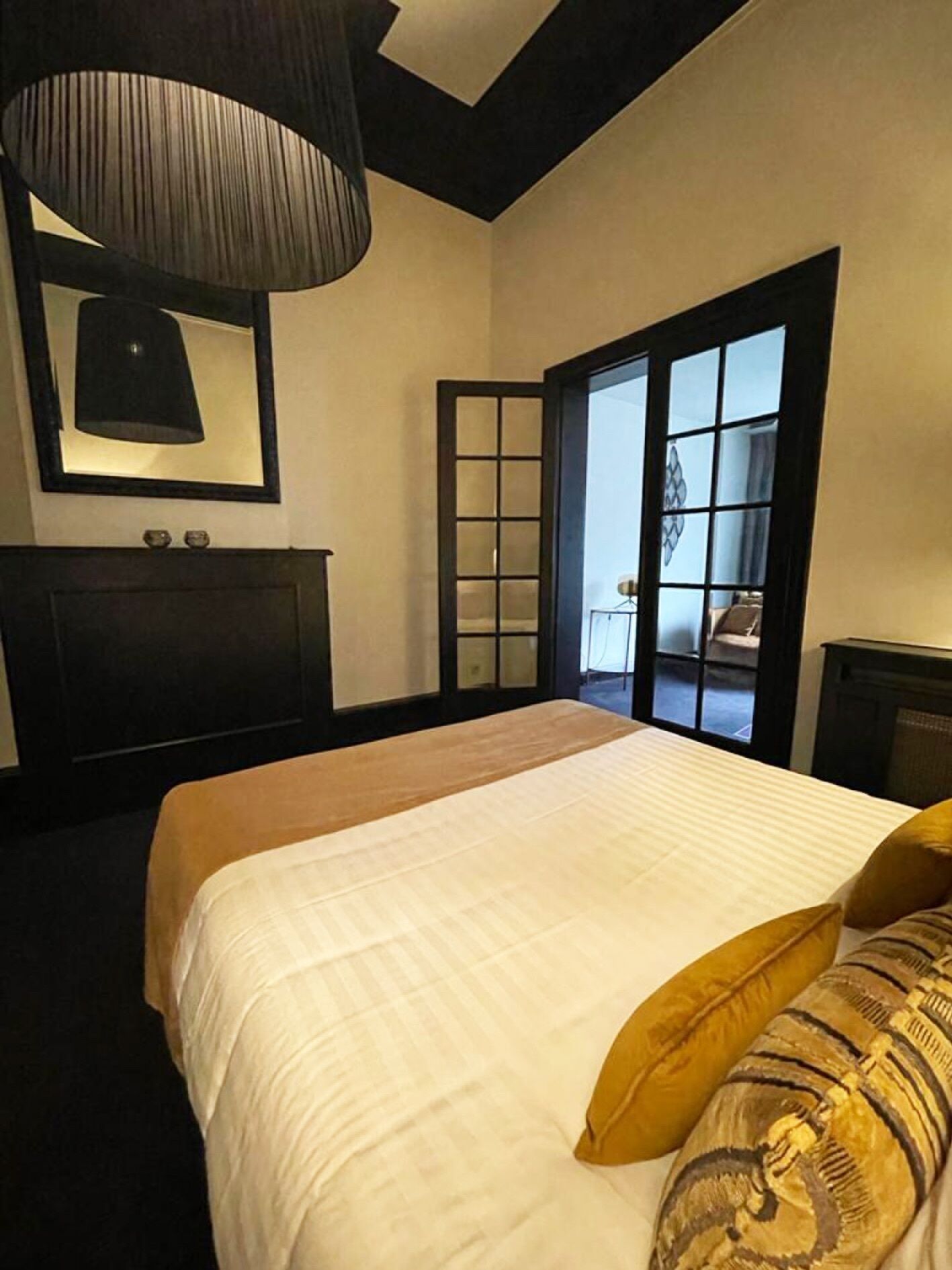 Un dormitorio con una cama grande, un cabecero oscuro, un espejo y una ventana con vistas.