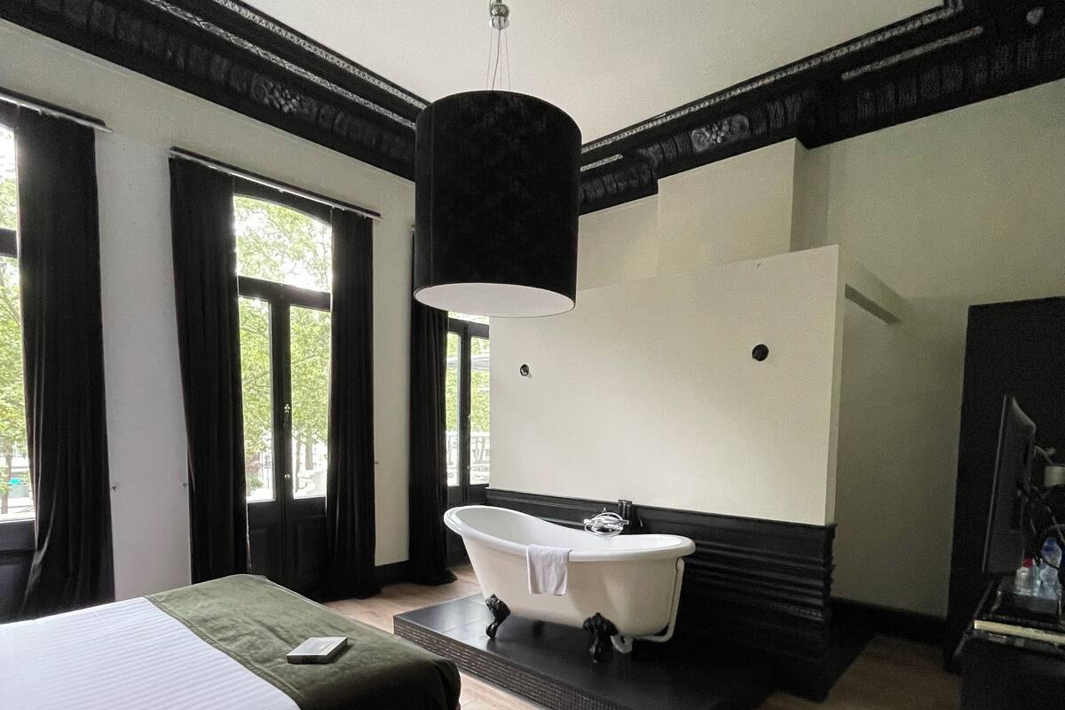 A hotel room with a large bed, a sitting area, a bathtub, and a mirror.
