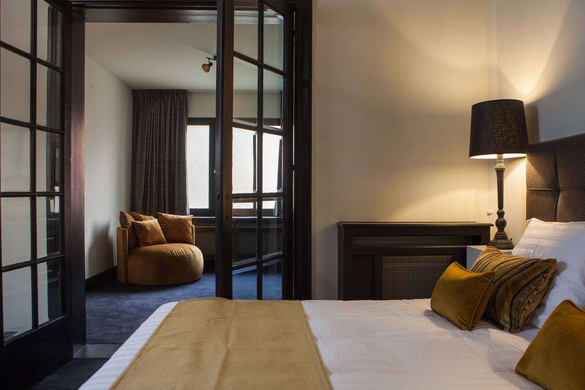 A hotel room with a bed, a seating area, a lamp, and a view through a glass door.