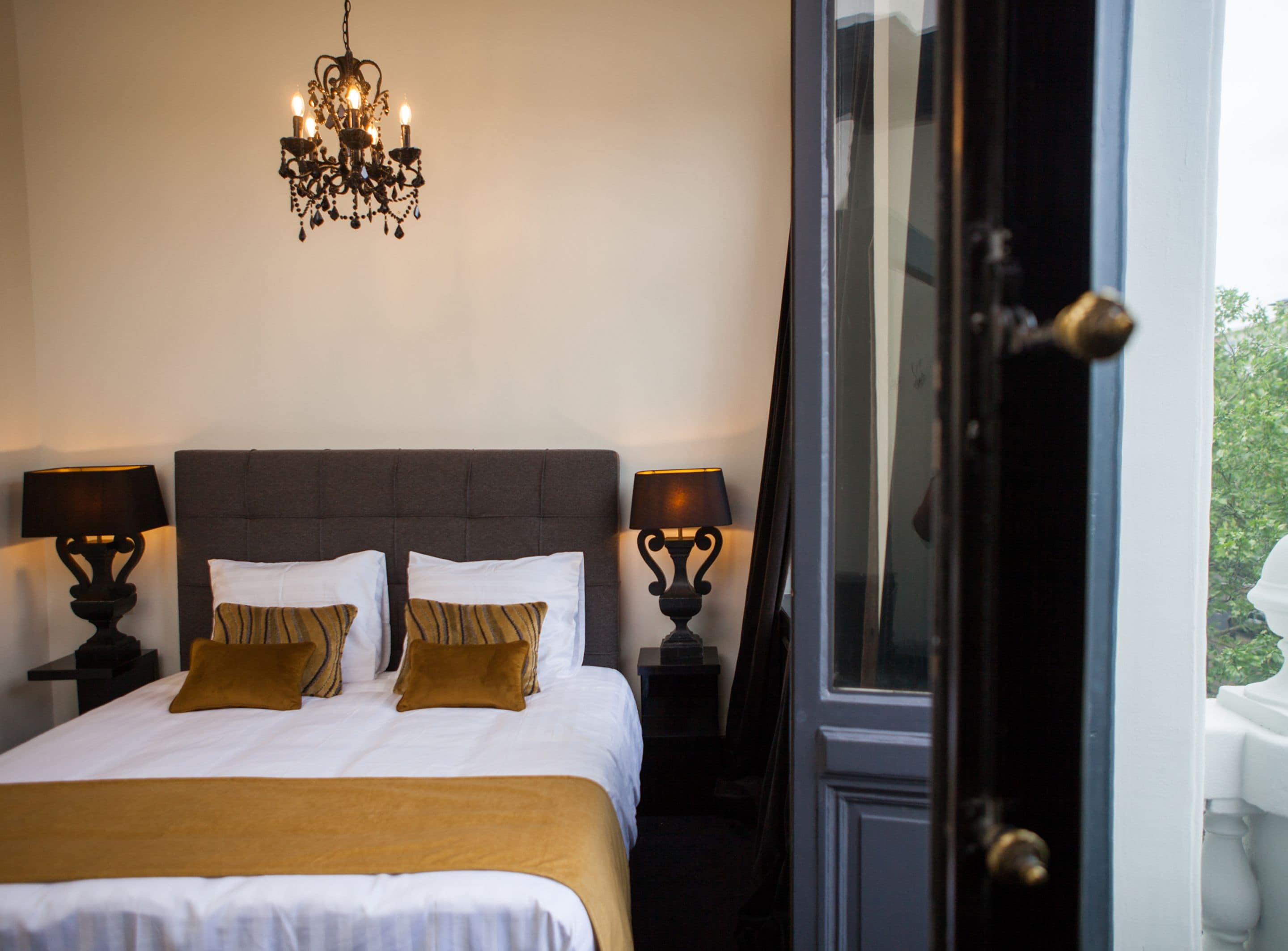 Une chambre à coucher avec un grand lit, deux tables de chevet, un lustre et une porte donnant sur l’extérieur.