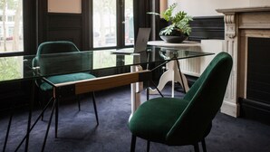 Una habitación moderna con una mesa de vidrio, una computadora portátil, una silla verde y una chimenea.