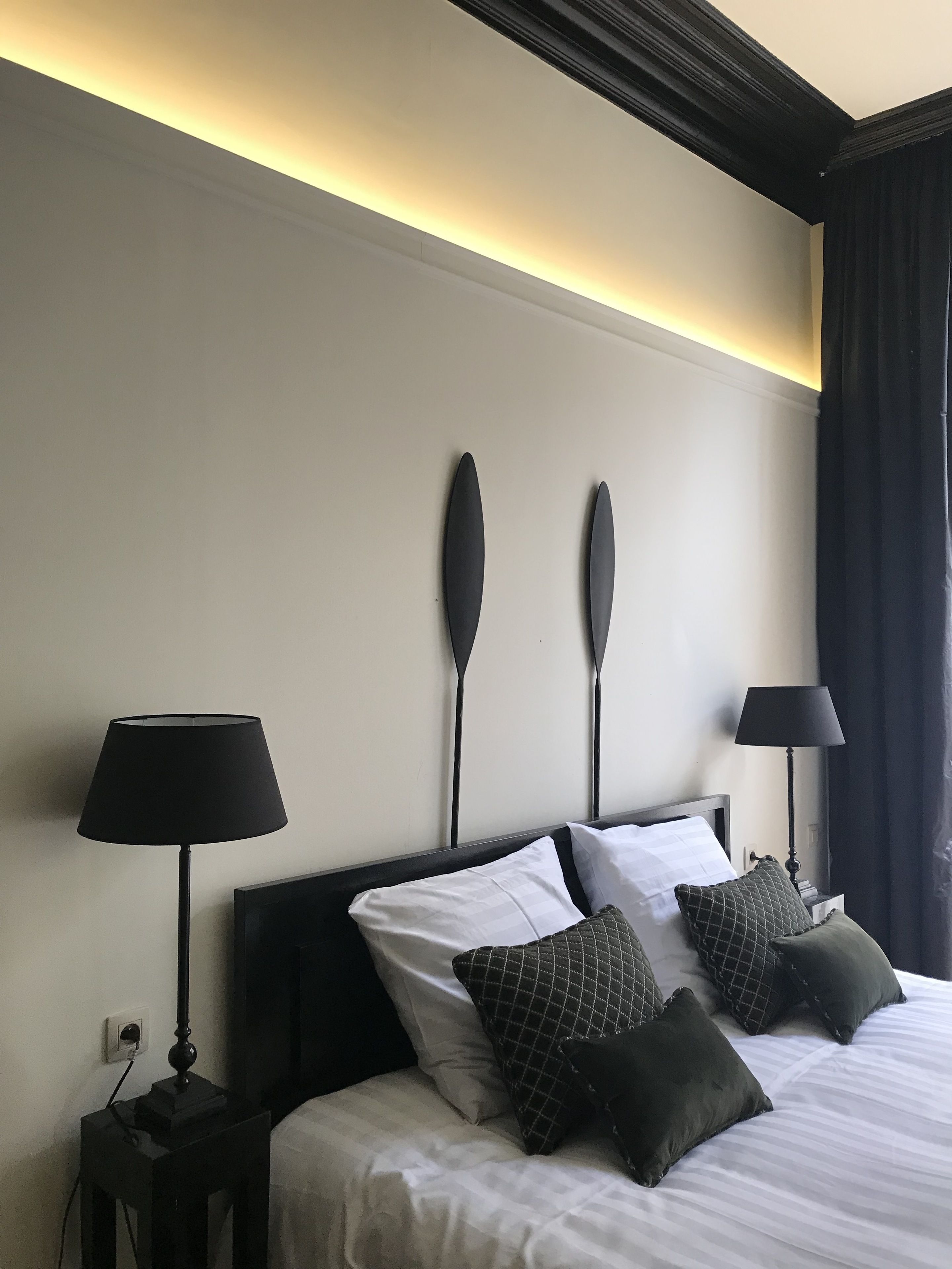 A hotel room with a bed, two bedside lamps, a wall-mounted light fixture, and a window with curtains.