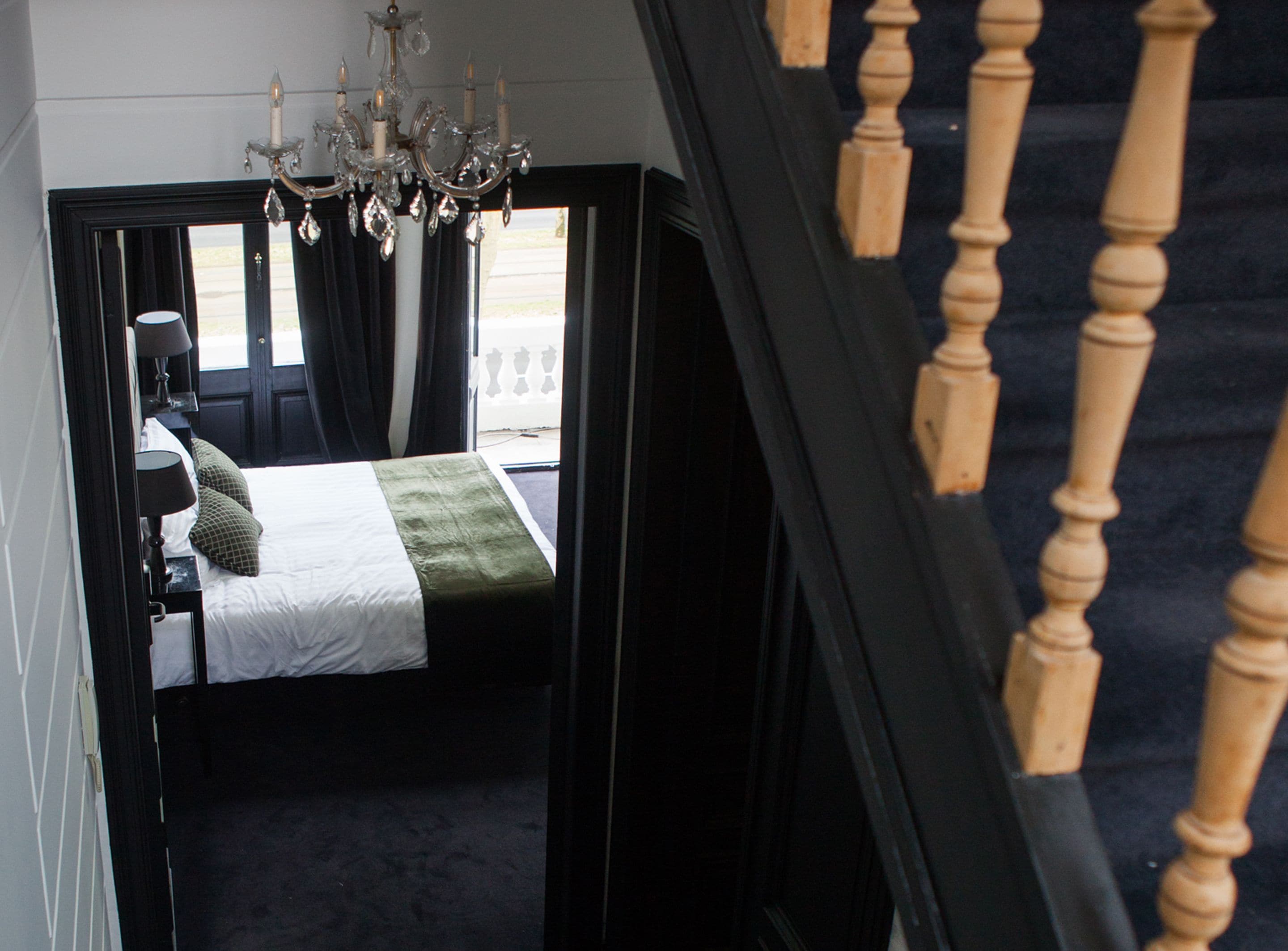 A bedroom with a bed, a chandelier, and a view through a window.