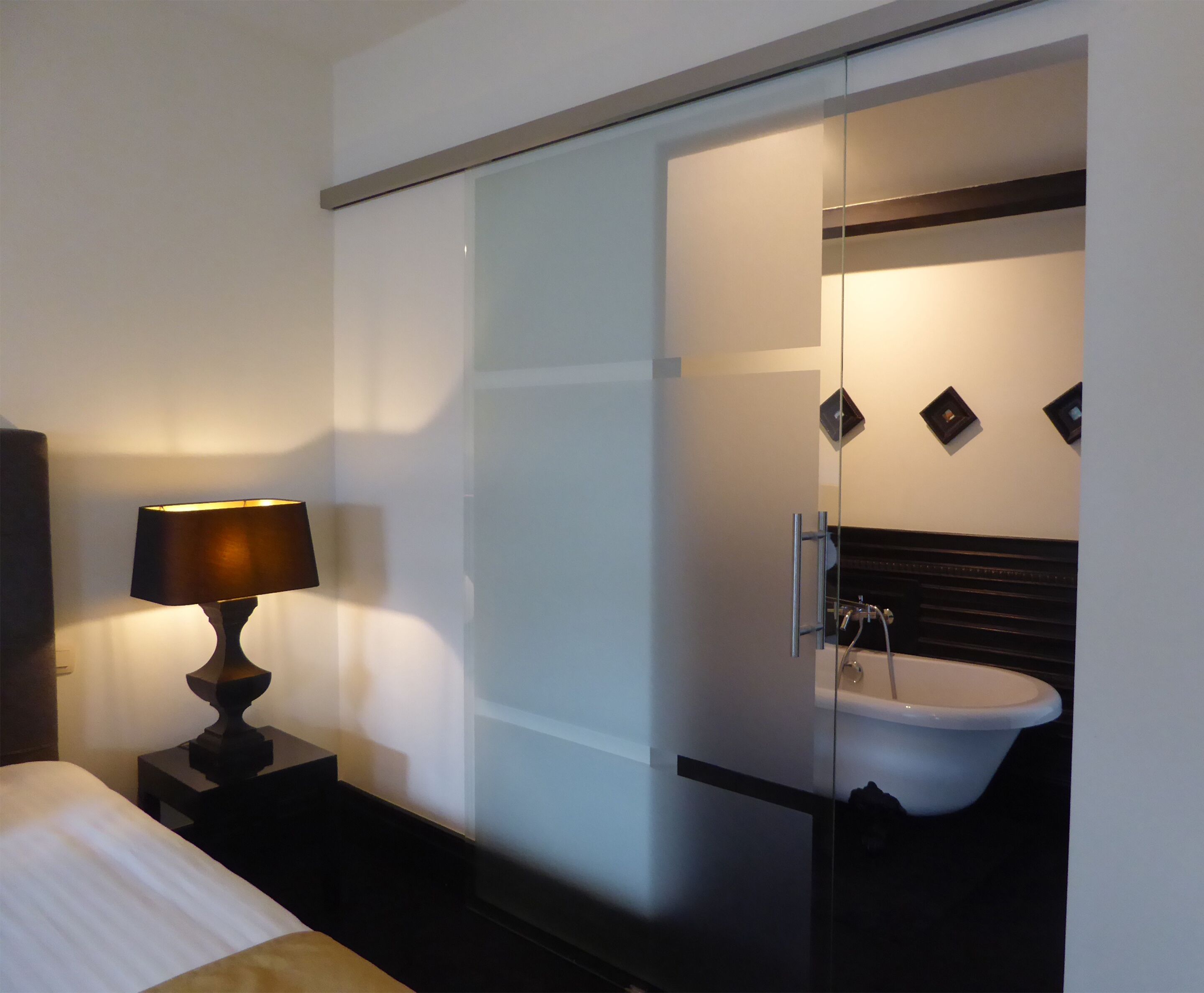Habitació d'hotel amb llit, làmpada de nit, boxa de dutxa de vidre i un lavabo.