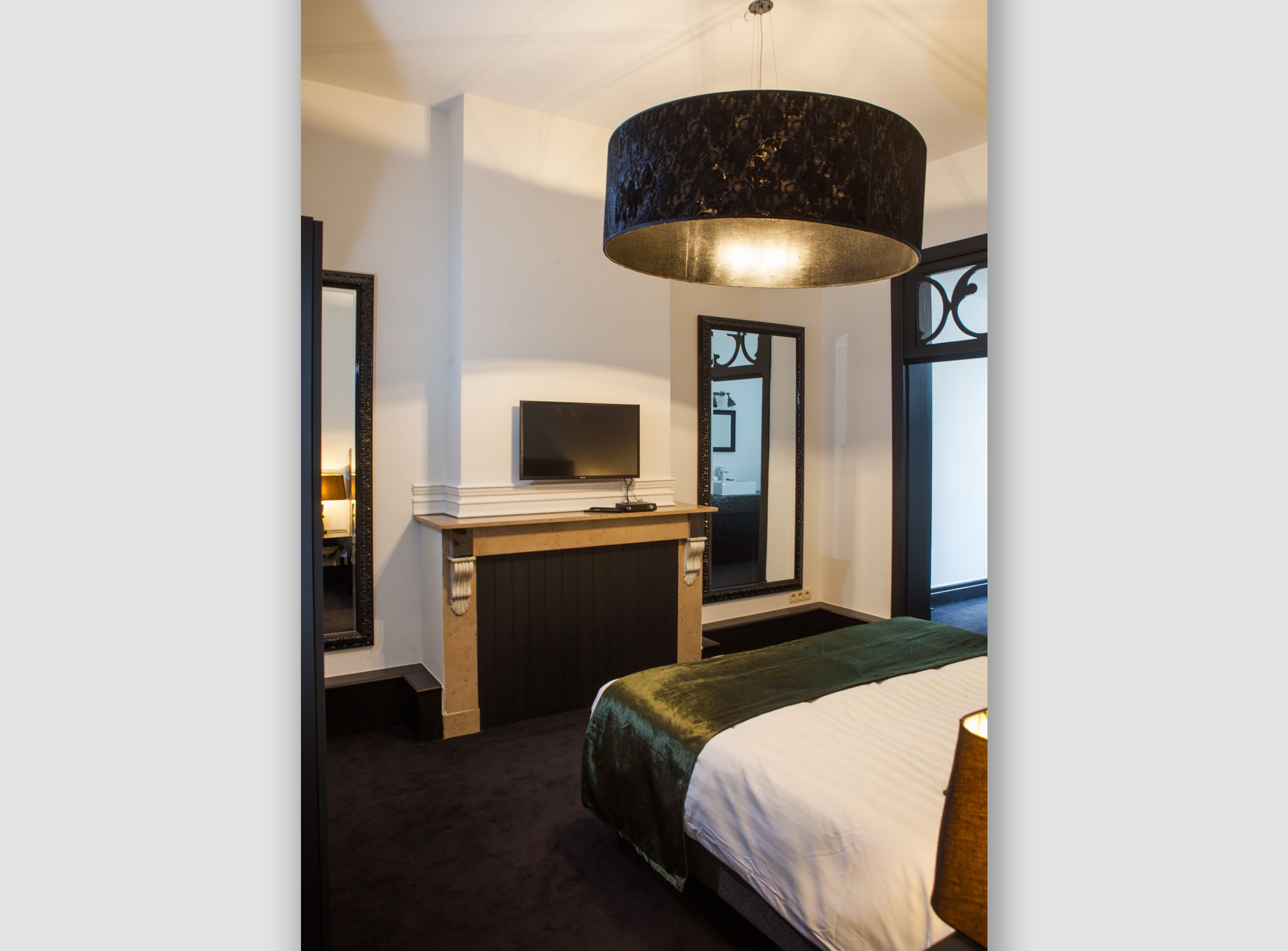 A modern hotel room with a large bed, a flat-screen TV mounted on a wooden console, a large mirror, and a black-framed window.