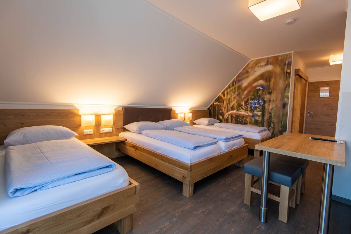 A modern bedroom with two beds, a wooden desk, and a small bench.