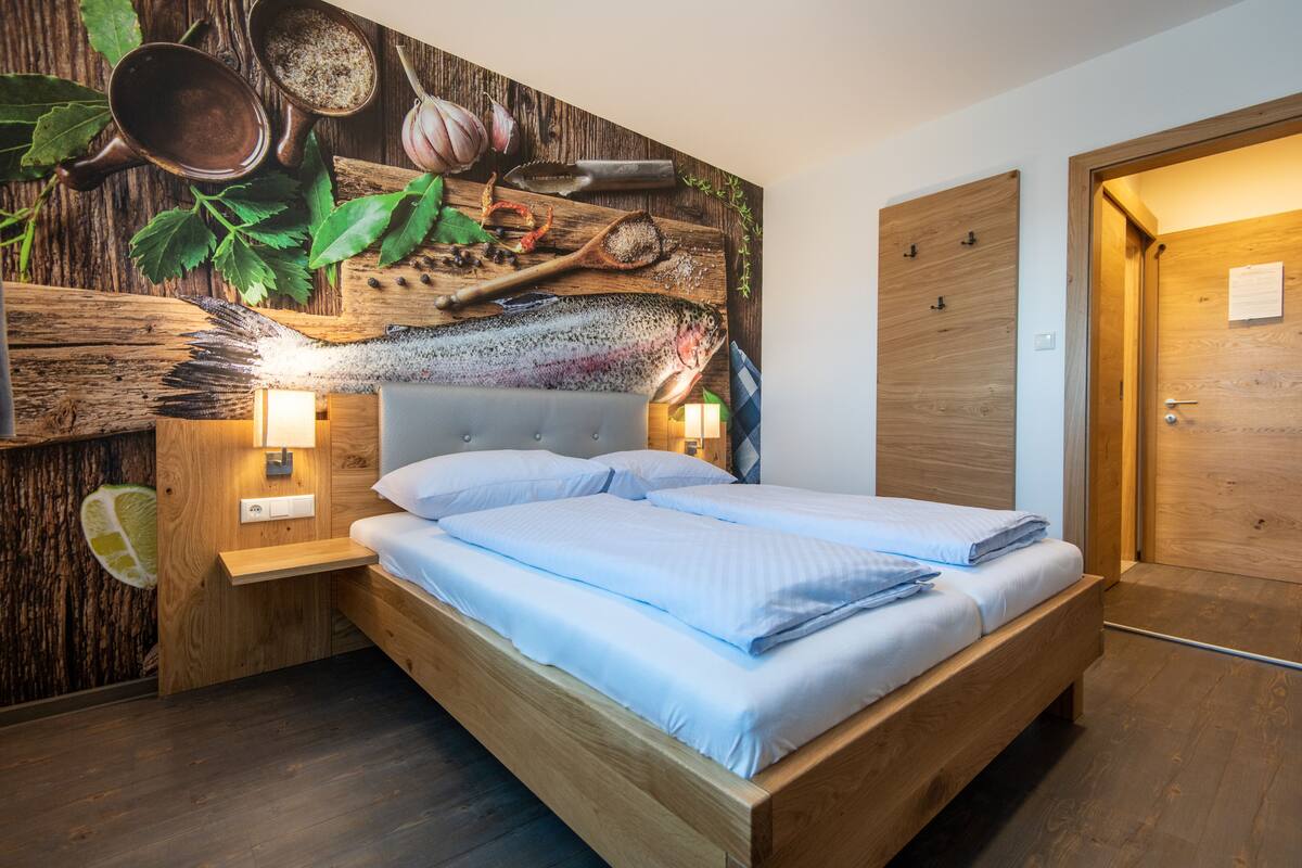 A modern bedroom with a wooden bed, a nightstand, and a wall mural of kitchen ingredients.