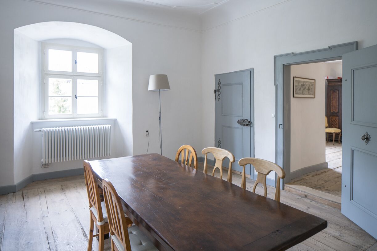 Ein Esszimmer mit Holztisch und -stühlen, einem Fenster mit Heizkörper und einer Lampe.