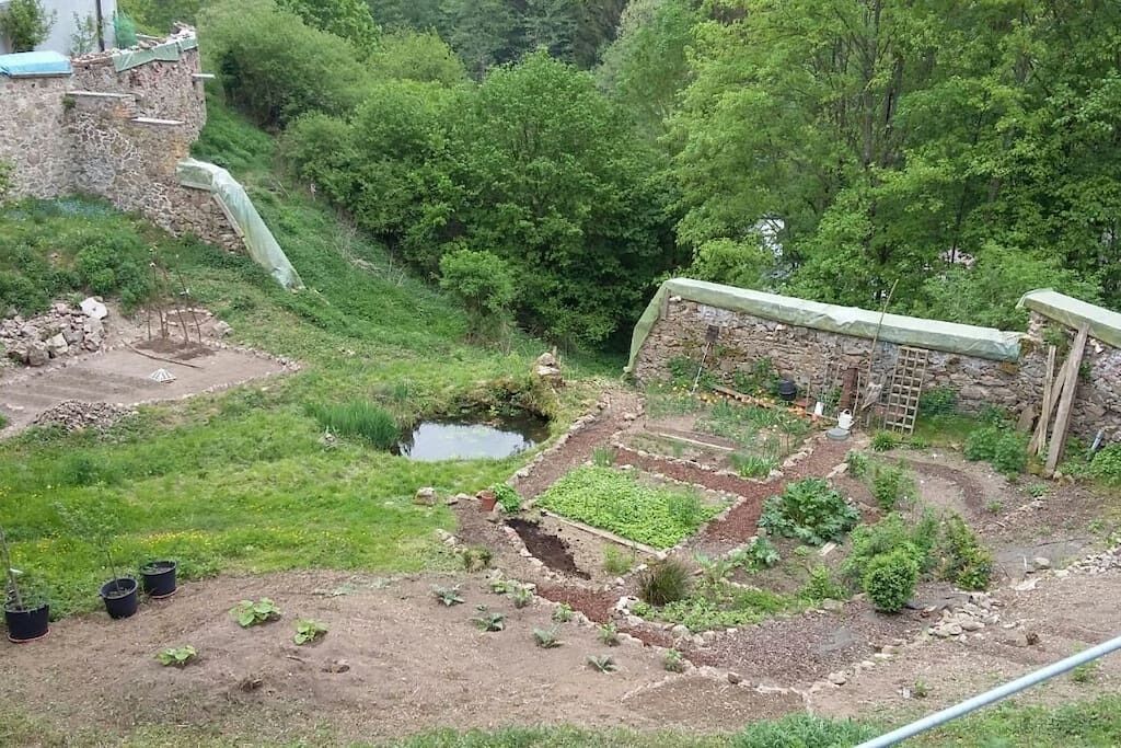 Ein Garten mit erhöhten Blumenbeeten, einem kleinen Teich und einer Steinmauer.