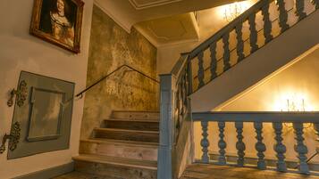 Eine Treppe mit Holzboden und blauen Geländern, ein gerahmtes Porträt an der Wand und eine Tür mit einer verzierten Griffstange.