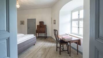 Une pièce avec un lit, une commode en bois, un bureau avec des livres et une fenêtre.