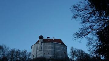 Ein großes, historisches Gebäude mit einem runden Turm und einem roten Dach, umgeben von Bäumen.