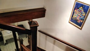 A wooden staircase with a handrail, a white wall, and a framed painting of a building.