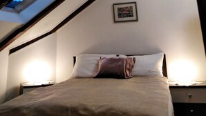A bedroom with a sloped ceiling, a bed with pillows, a nightstand, and a framed picture on the wall.