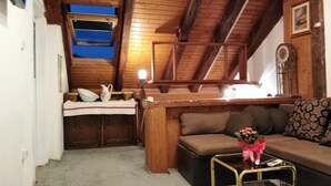 A cozy room with a wooden ceiling, a sofa, a small table with a vase of flowers, and a window with a view.