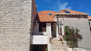 A building with a stone facade, a tiled roof, and a small garden with red flowers.