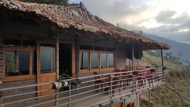 A rustic building with a thatched roof and a balcony with red chairs. - Thanh Homestay (Sa Pa)