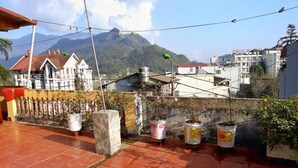 A rooftop terrace with potted plants, a view of a mountain, and buildings in the background. - Thanh Homestay (Sa Pa)