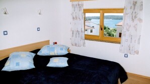 A bedroom with a bed, two pillows, a window with curtains, and a view of a body of water and buildings.