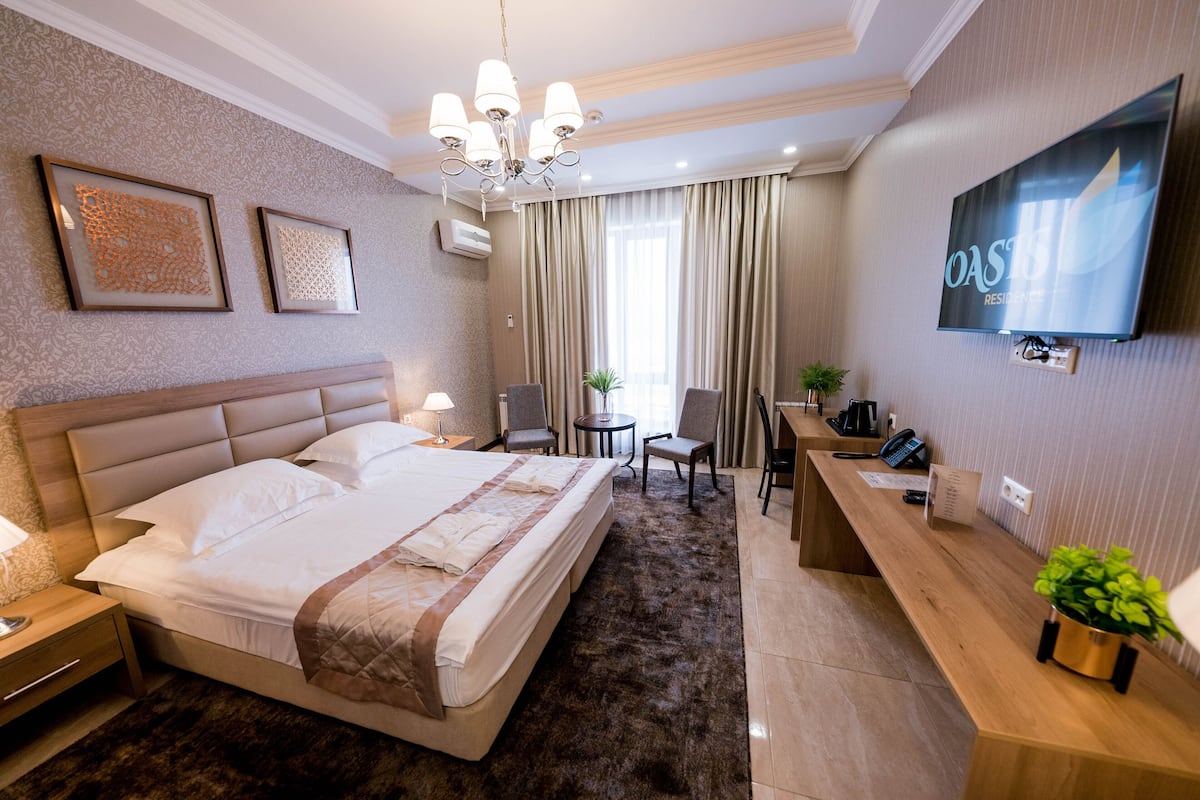 A hotel room with a large bed, a desk, a chair, a TV, and artwork on the wall.