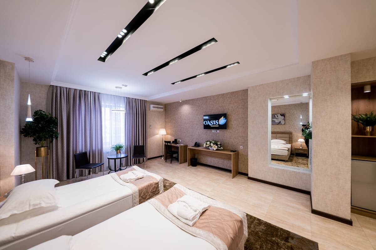 A hotel room with two beds, a desk, a TV, and a mirror.