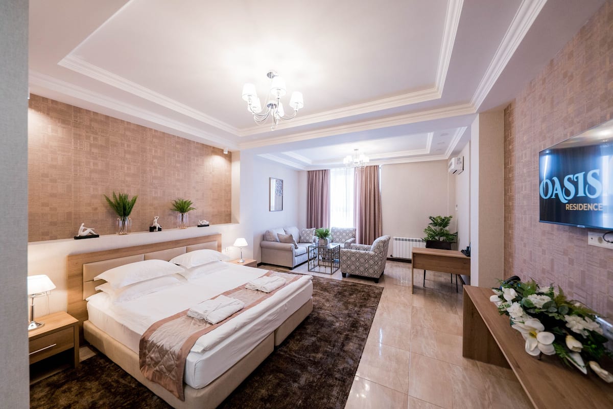 A modern hotel room with a large bed, a desk, a sofa, and a TV.