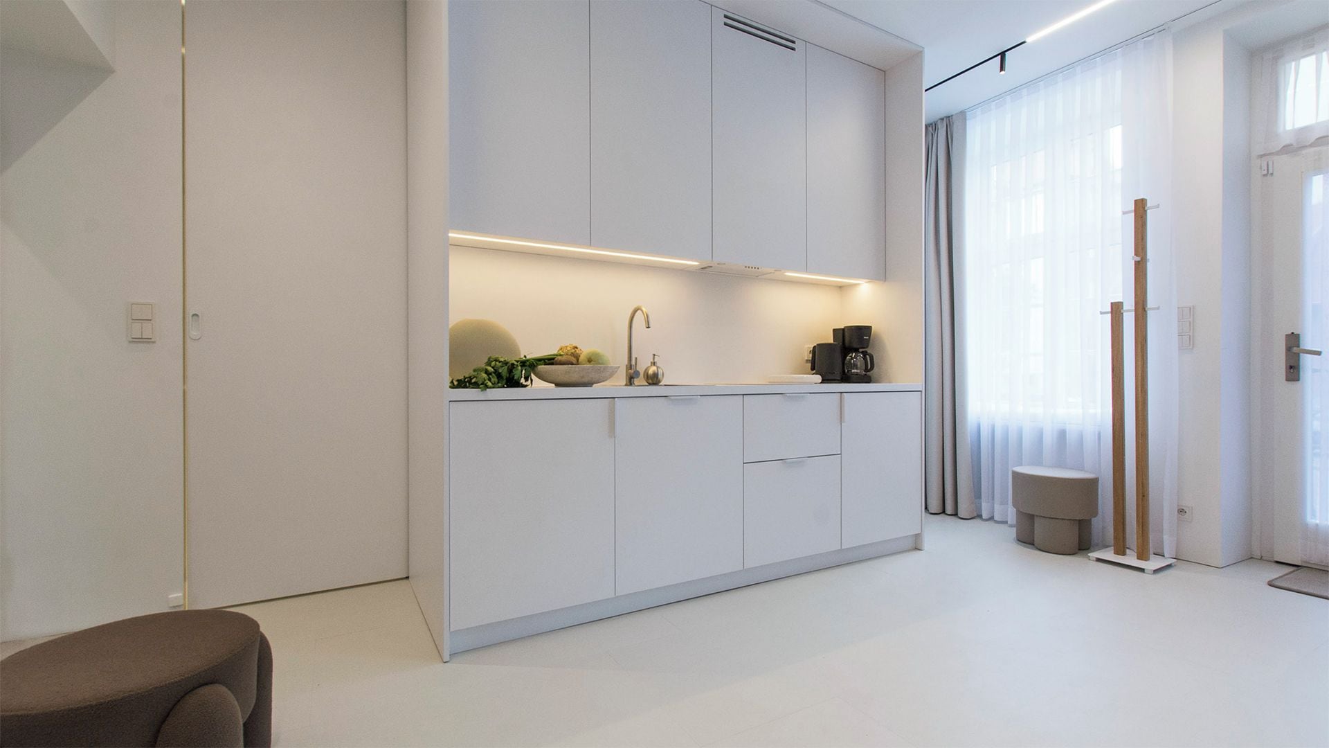 Una cocina moderna con armarios blancos, horno empotrado y cafetera sobre la encimera.