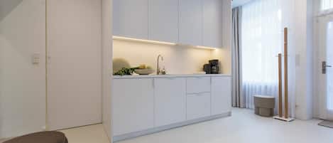 Una cocina moderna con armarios blancos, horno empotrado y cafetera sobre la encimera.