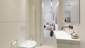 Un bany modern amb un vàter blanc, un lavabo amb dispensador de sabó i una zona de dutxa.