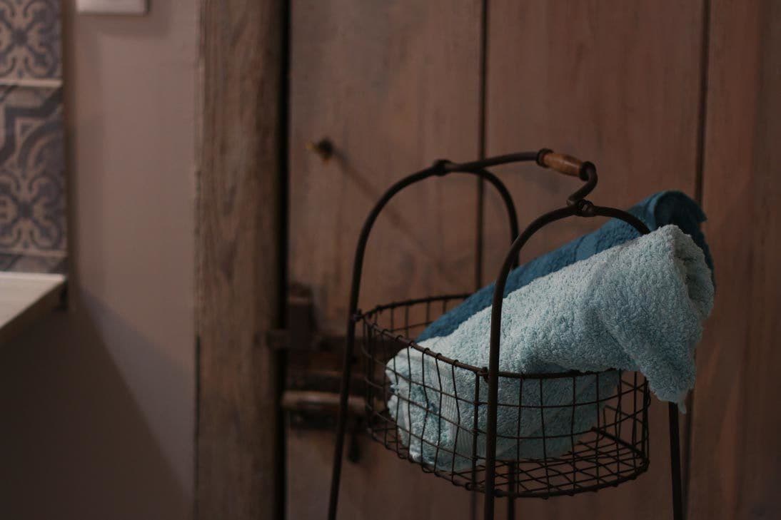 Een metalen mand met een blauwe handdoek, hangend aan een wandrek in een kamer met houten lambrisering.