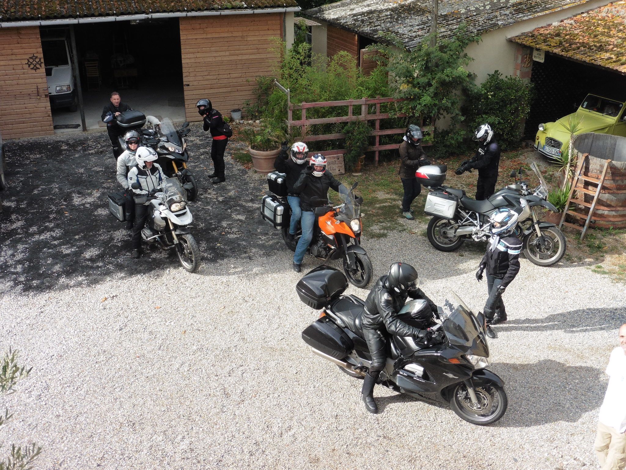 A group of motorcyclists gathered outside a building with a gravel driveway.