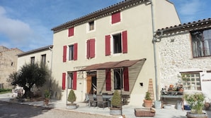 A two-story building with red shutters, a covered entrance, and outdoor seating with potted plants.