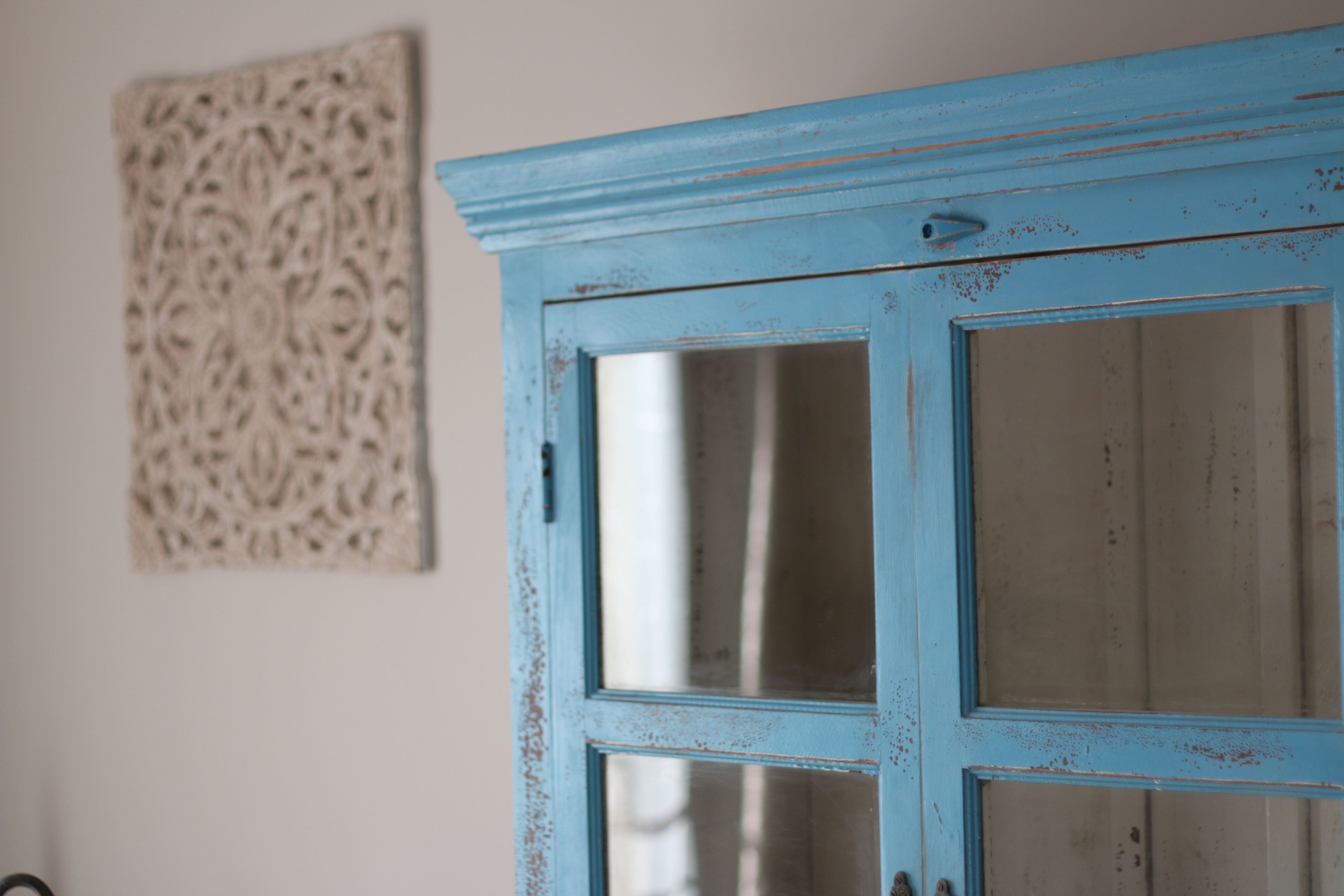 Una puerta azul con paneles de vidrio, una obra de arte en relieve en la pared y una pared lisa.
