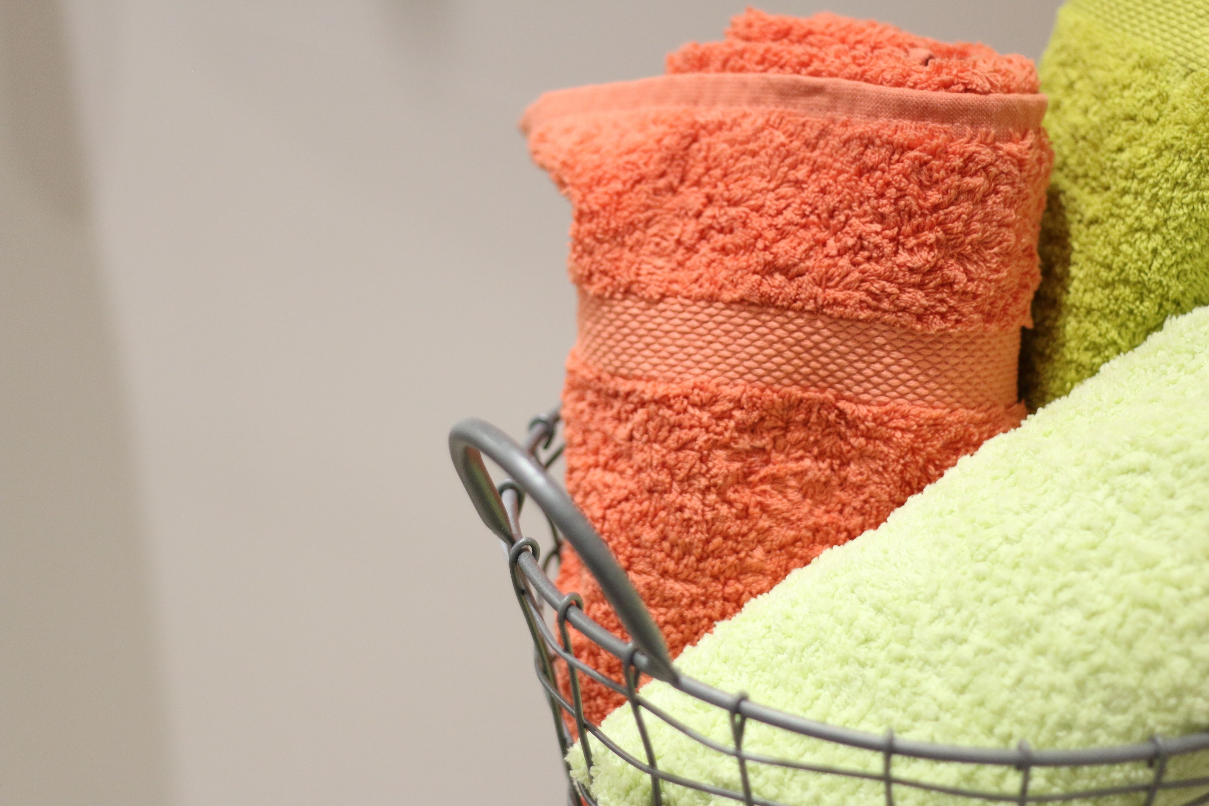 A metal basket containing three towels in different colors.