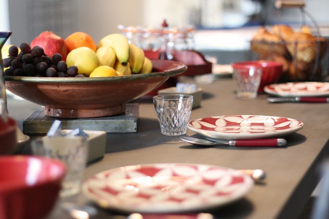 A buffet table with a variety of fruits, plates, and glasses.
